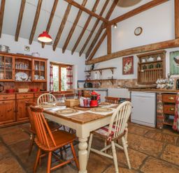 A kitchen with wooden dining table and chairs wooden cabinets and exposed ceiling beams at Downs View Dairy in West Tytherley