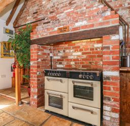 A kitchen with a large stove built into a brick fireplace and a green plant in a pot at Downs View Dairy in West Tytherley