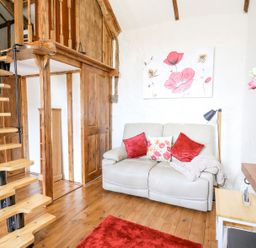 A small living room with a beige couch red cushions a wooden spiral staircase and floral wall art at Rose Cottage in Penrhiwllan