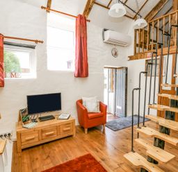 A living room with a wooden tv stand and television red armchair spiral staircase and wooden floor at Rose Cottage in Penrhiwllan