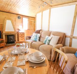 A living room with a dining table set with dishes and glasses a sofa and armchair with cushions a fireplace and a television at Brook Lodge in Penrhiwllan