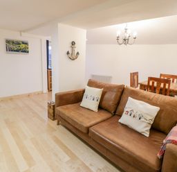 A living room with a brown leather sofa and wooden dining table with chairs at Pentowyn in Holyhead