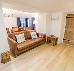 A living room with a brown leather sofa and dining table with chairs near windows at Pentowyn in Holyhead