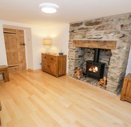 A living room with a stone fireplace wooden furniture and a wood burning stove at Pentowyn in Holyhead