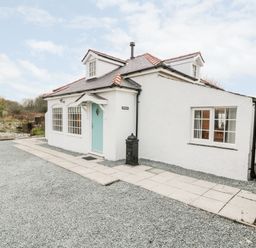 A white house with a blue door and two dormer windows on a gravel driveway at Pentowyn in Holyhead