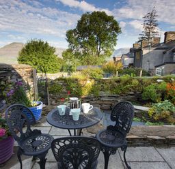 An outdoor patio area with a metal table and three chairs with cups and a French press surrounded by plants and stone walls at Moelwyn View Cottage in Llan Ffestiniog