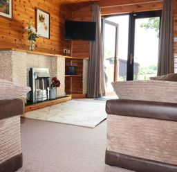 A living room with wood paneled walls a fireplace a mounted television and two sofas at Oak Lodge Constantine near Falmouth