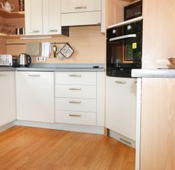 A kitchen with white cabinets a toaster kettle oven and bread bin at Oak Lodge in Constantine near Falmouth