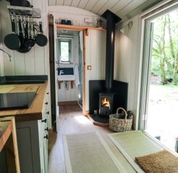 A compact kitchen area with wooden countertops pots and pans hanging and a stove next to a wood burning stove at Rock View Shepherd's Hut in Gulworthy near Tavistock