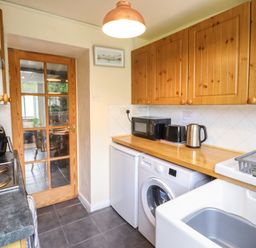 A kitchen with wooden cabinets a washing machine a mini fridge microwave toaster kettle and a sink at Gwenallt in Malltraeth