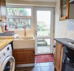 A kitchen with a washing machine sink and oven next to a door leading outside at Gwenallt in Malltraeth