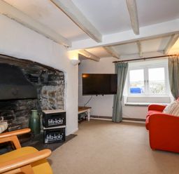 A living room with a stone fireplace wooden chairs a red sofa a wall-mounted television and a window with curtains at Lanvean Farmhouse Lanvean near St Mawgan