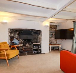 A living room with chairs a fireplace and a television at Lanvean Farmhouse in Lanvean near St Mawgan