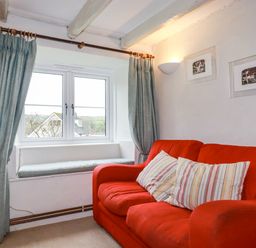 A living room with a red sofa and striped pillows next to a window with blue curtains at Lanvean Farmhouse in Lanvean near St Mawgan
