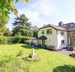 A garden with grass and trees next to a white house with a stone extension at Coed Derw Isaf in Betws-Y-Coed