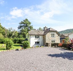 A stone and white painted house with a gravel driveway and garden at Coed Derw Isaf in Betws-Y-Coed