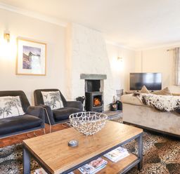 A living room with two chairs a coffee table a fireplace a sofa and a television at Coed Derw Isaf in Betws Y Coed