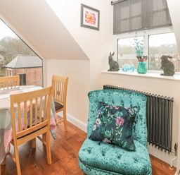 A dining area with wooden chairs and round table with tablecloth next to a window with rabbit figurines and a vase at River Cottage in Morpeth