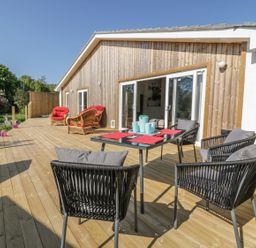 A wooden deck with black chairs and a table with turquoise vases and red placemats outside a wood-paneled house at Chy Lagen Hos in Newquay