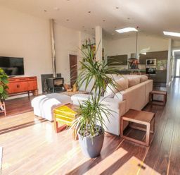An open living room with a gray sectional sofa a wooden sideboard a flat screen tv a wood stove and a large potted plant at Chy Lagen Hos in Newquay