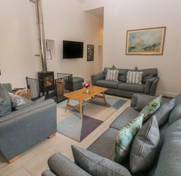 A sitting room with three sofas a wooden coffee table a rug a wall mounted tv a wood burning stove and framed pictures at The Old Carriage Court in Kidwelly