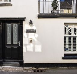 A black front door with glass panes next to a white wall with a window and a sign saying Serendipity at Serendipity in Fowey
