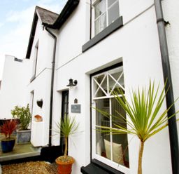Exterior view of a white house with potted plants near the window and door at The Shell Seekers in Fowey