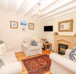 A living room with sofas and armchairs around a fireplace with a mirror above at The Shell Seekers in Fowey