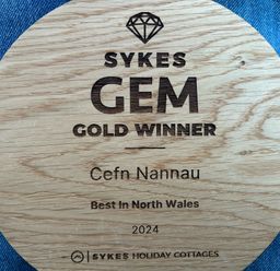 A wooden circular plaque awarded to Cefn Nannau for being the best in North Wales in 2024 placed on blue denim fabric