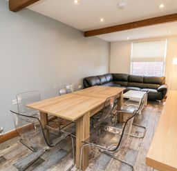 A dining area with a wooden table surrounded by transparent chairs and a black leather sectional sofa at 11A Church Street in Whitby