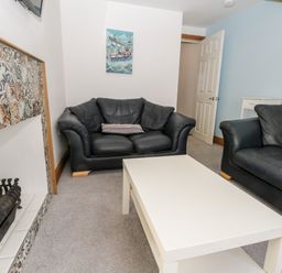 A living room with black sofas white coffee table and a tiled fireplace at 11A Church Street Whitby