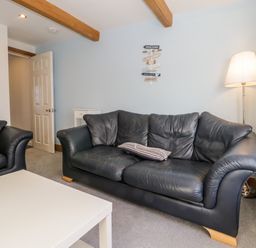A living room with black leather sofas a white coffee table a floor lamp and a sign on the wall at 11A Church Street in Whitby