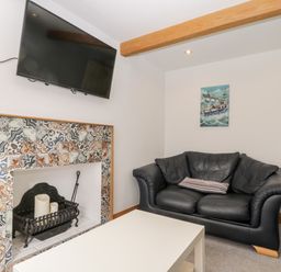 A living room with a black leather sofa a white table a tiled fireplace with candles and a wall mounted television at 11A Church Street in Whitby