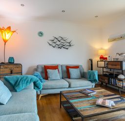 A living room with blue sofas red and blue cushions a wooden coffee table and decorative lamps at Tides Reach in Rhosneigr