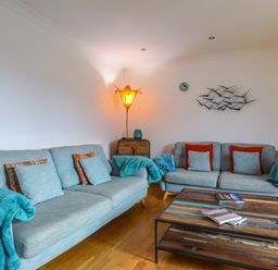 A living room with two blue sofas a wooden coffee table and a floor lamp at Tides Reach in Rhosneigr