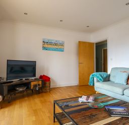 A living room with a television on a wooden stand and a blue sofa with cushions and a throw at Tides Reach in Rhosneigr