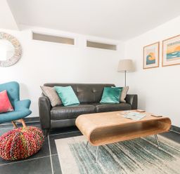 A living room with a black sofa teal armchair wooden coffee table and wall art at Gull Rock Trebarwith Strand