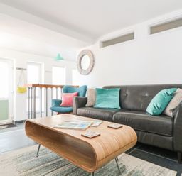 A living room with a black sofa with pillows a wooden coffee table and a blue armchair at Gull Rock in Trebarwith Strand