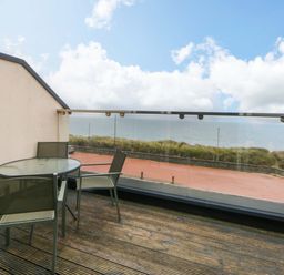 An outdoor balcony with a table and chairs overlooking the sea at Welymora Pwllheli