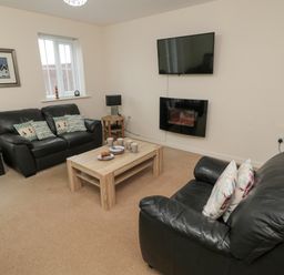 A living room with two black leather sofas a wooden coffee table mugs on the table a wall-mounted TV and electric fireplace at Beach House in Beadnell