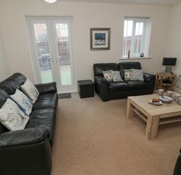 A living room with two black leather sofas a wooden coffee table with cups and plates and a side table with a lamp at Beach House in Beadnell