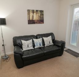 A black leather sofa with three decorative pillows a floor lamp a wall painting and glass doors with blinds at Beach House in Beadnell