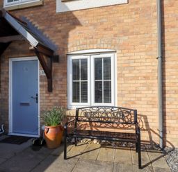 A blue front door with a small roof above and a black metal bench with welcome sign outside a brick house