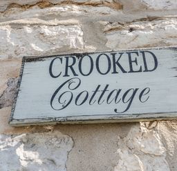 A wooden sign with the text Crooked Cottage on a stone wall at Crooked Cottage in Kirkbymoorside