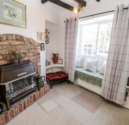 A sitting area with a brick fireplace bench with cushions and a window with curtains at Crooked Cottage in Kirkbymoorside