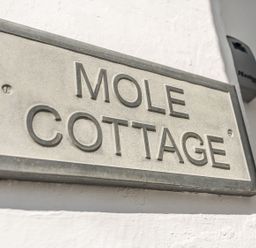 A sign on a white wall displaying Mole Cottage in Mousehole