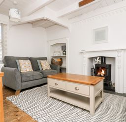 A living room with gray sofas a wooden coffee table a fireplace and a patterned rug at Mole Cottage in Mousehole