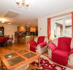 A living room with two armchairs covered with red throws a wooden coffee table and a dining table with chairs next to a kitchen area at Vine Lodge in Kingsbury Episcopi near Martock