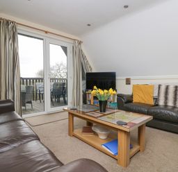 A living room with leather sofas a glass top coffee table and a television near sliding glass doors at Valley Lodge 48 in Callington