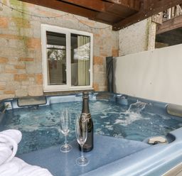 An outdoor hot tub with water flowing and a bottle with two glasses and a white towel at Valley Lodge 48 in Callington